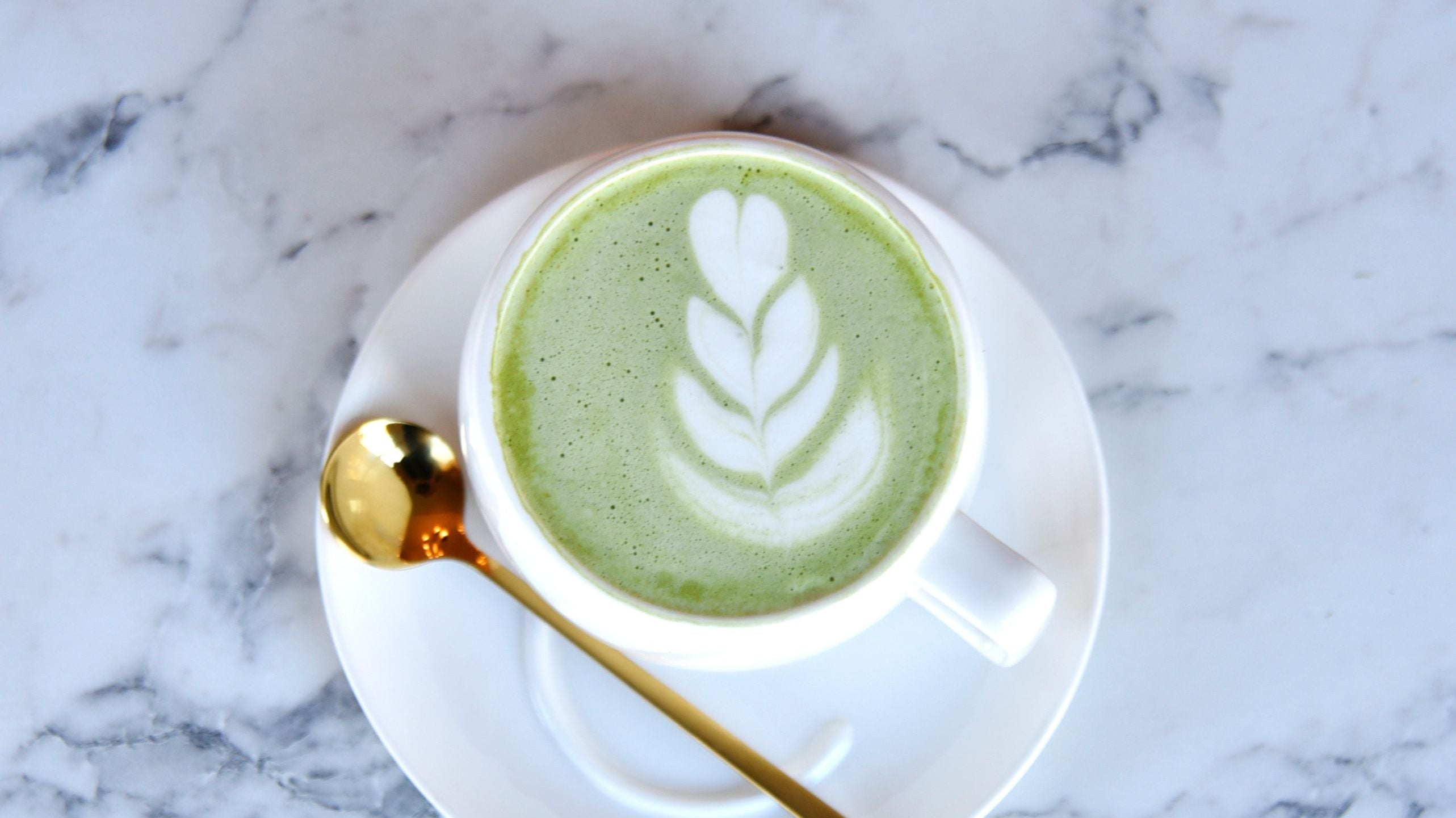 Matcha latte in cup with gold spoon on marble surface