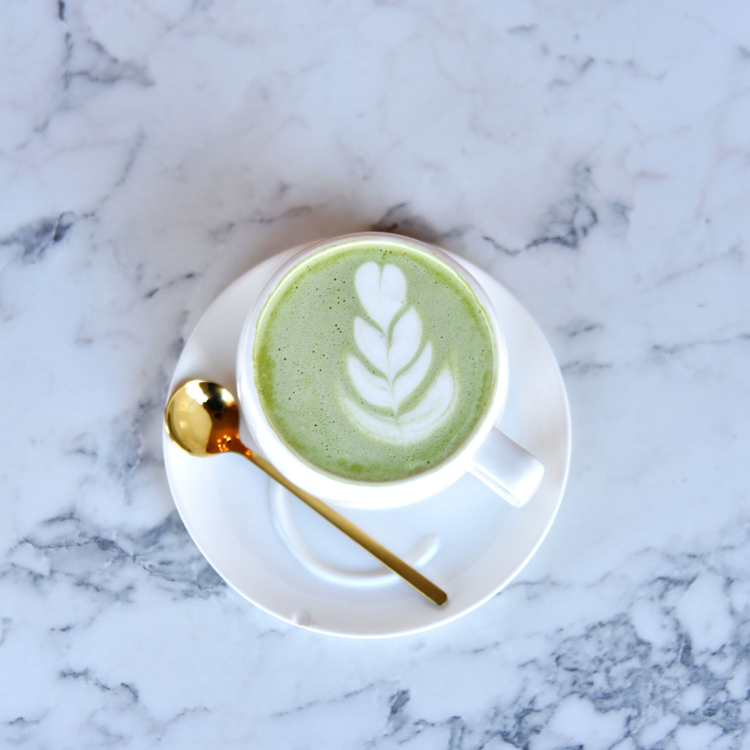 Matcha latte in cup with gold spoon on marble surface